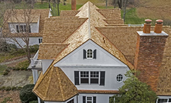 New golden-brown cedar shake roof on a classic colonial home with brick chimneys.