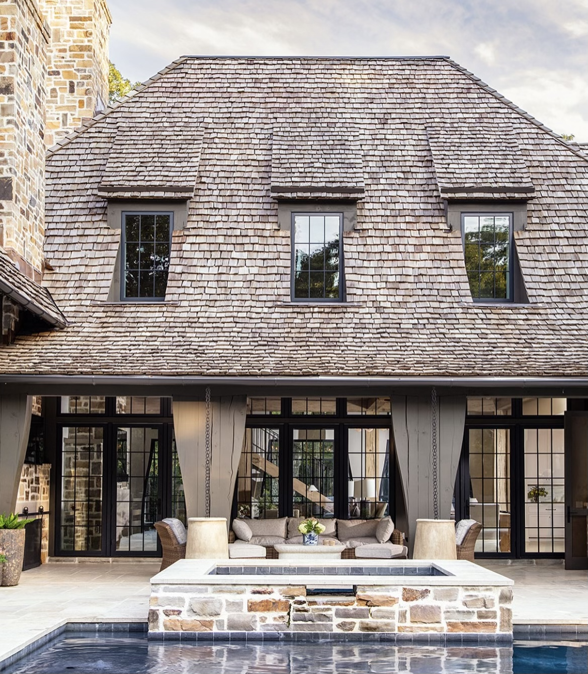 A beautifully weathered cedar shake roof on a stone home overlooking a luxury pool and patio.