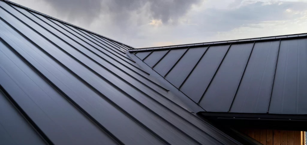 Close-up of a dark standing seam metal roof under a cloudy sky.