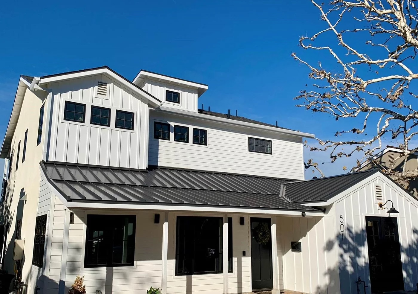 Sleek dark standing seam metal roof on a modern white farmhouse.