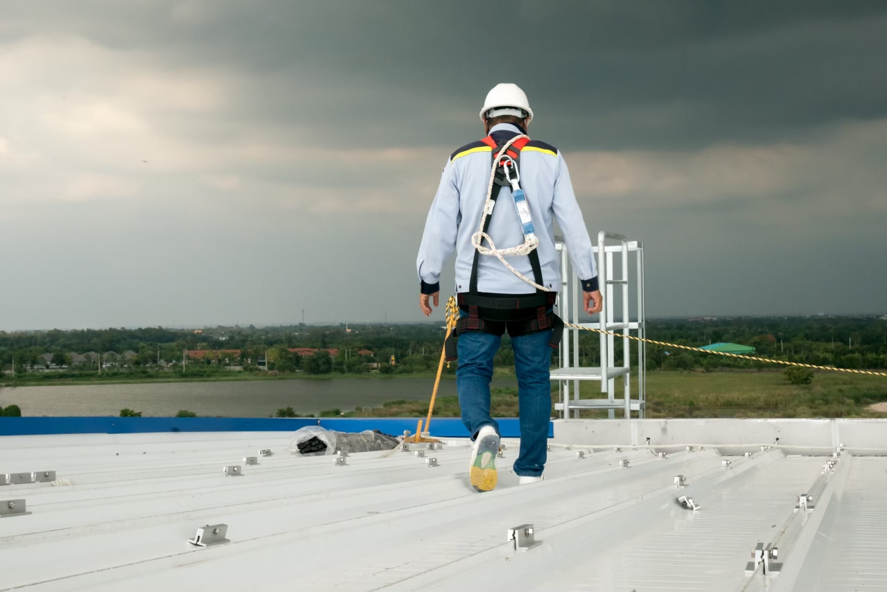 Roofer in safety gear inspecting a large commercial roof under a stormy sky.