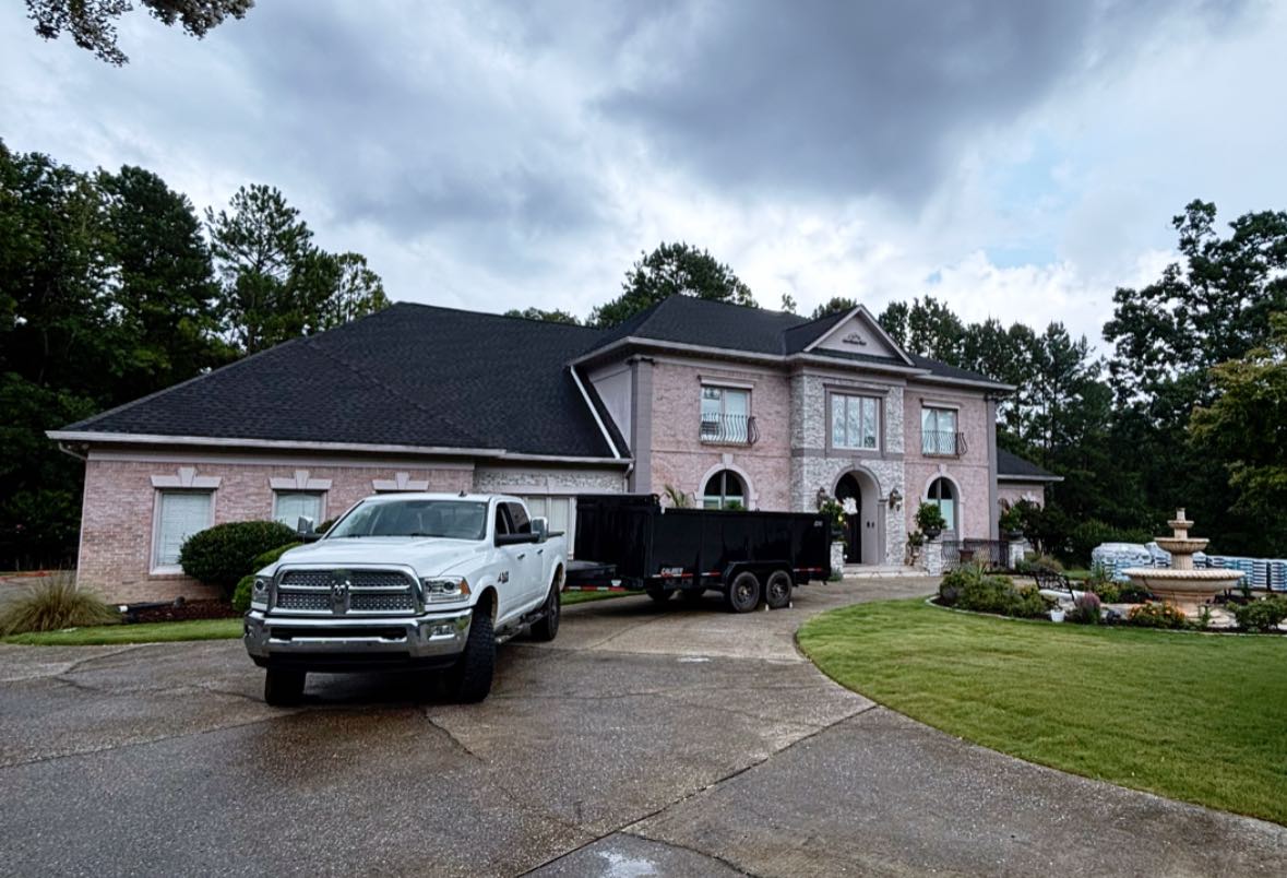 New dark architectural shingle roof on a beautiful pink brick home with a circular driveway and fountain.