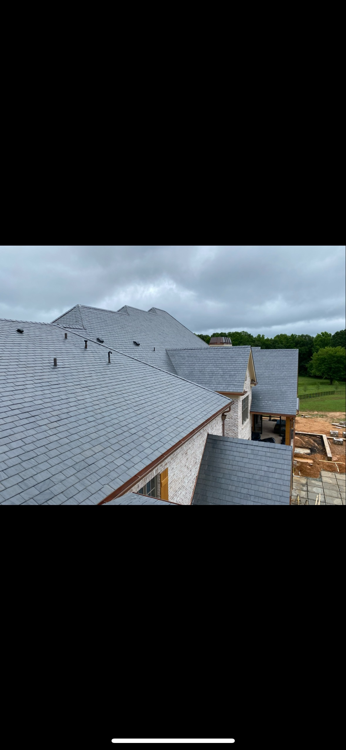 Side-angle view of a new grey slate roof on a home under construction.