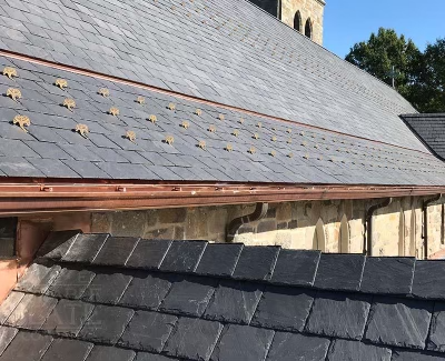 Durable slate roof with copper gutters and snow guards on a classic stone building.